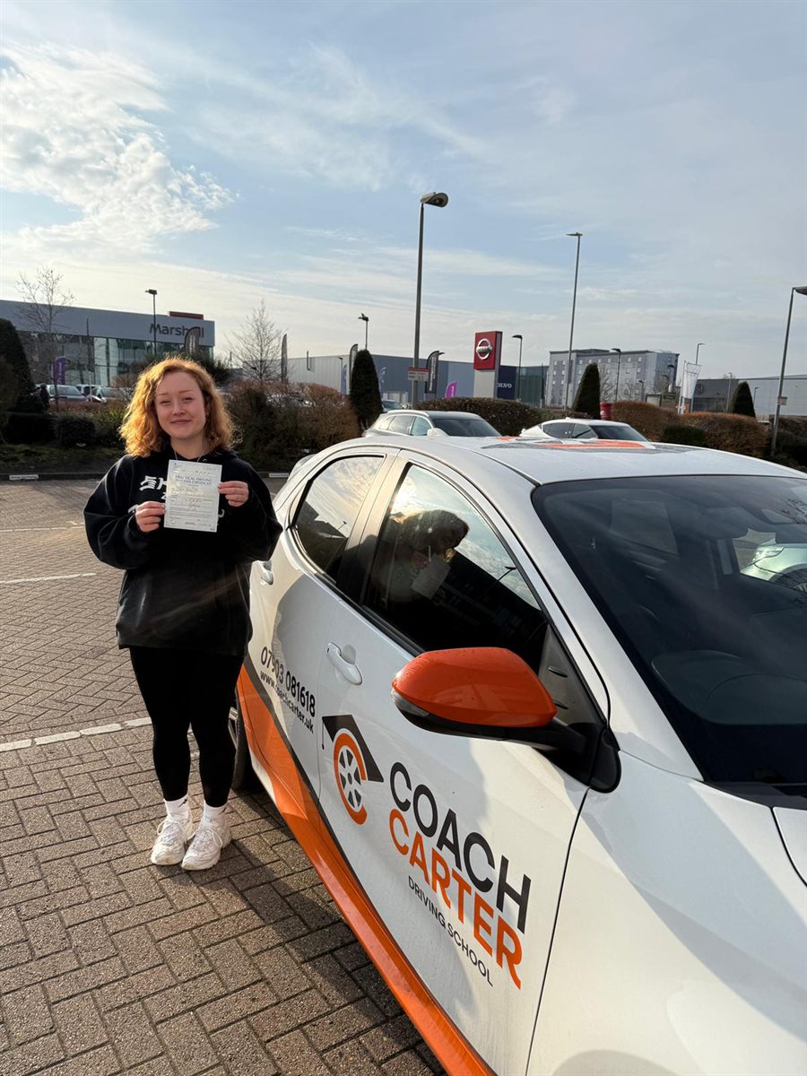 Olivia holding her pass certificate next to the CoachCarter car